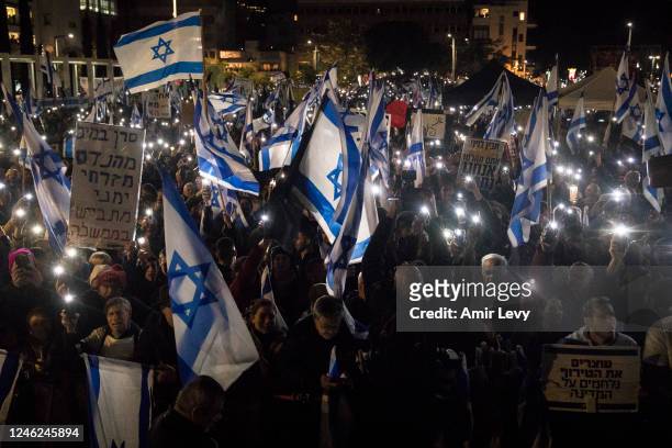 Israelis hold the Israeli flag and light their phones as they protest against the new Israeli far-right government on January 14, 2023 in Tel Aviv,...
