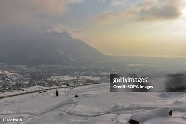 Man walks along the snow covered hill after a fresh snowfall on the outskirts of Srinagar. Weather improved in Kashmir valley after days of moderate...