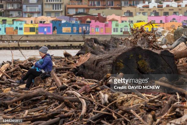 Woman sits with her baby among trees that were swept into the ocean by recent storms and washed ashore on the beach in Capitola, California, on...