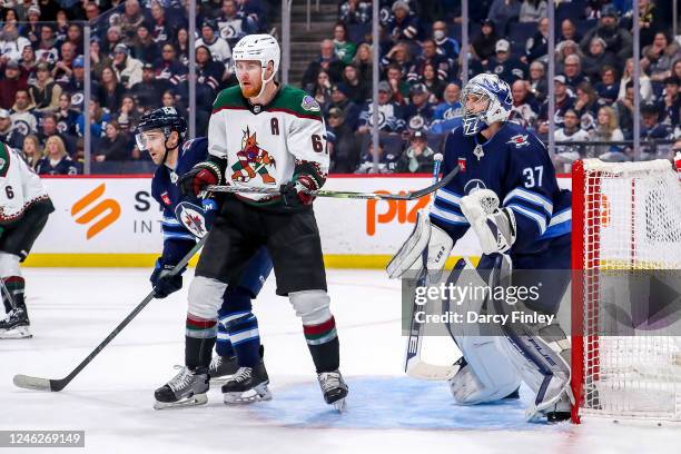 Neal Pionk of the Winnipeg Jets battles Lawson Crouse of the Arizona Coyotes in front of goaltender Connor Hellebuyck as they keep an eye on the play...