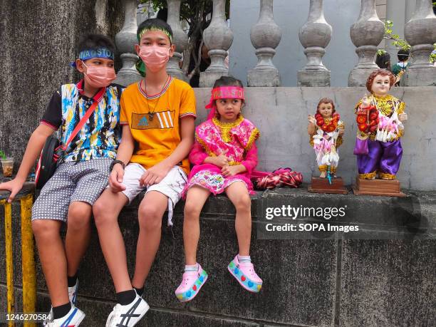 Three siblings wearing headbands sit with their Señor Santo Niño replicas outside the Santo Niño de Tondo Parish. Catholic devotees flock to Santo...