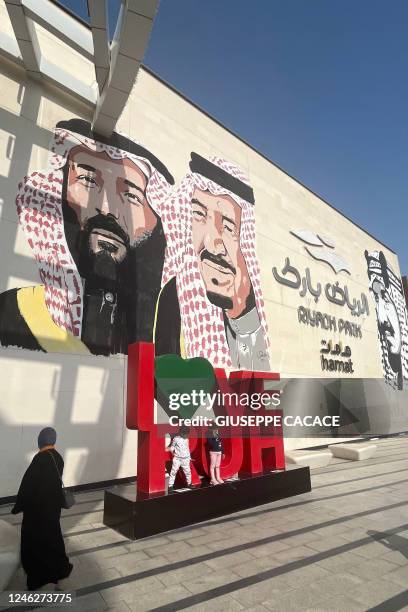 Saudi woman stands near a mural depicting Saudi King Salman bin Abdulaziz , Crown Prince Mohammed and King Abdulaziz bin Saud , the founder of the...