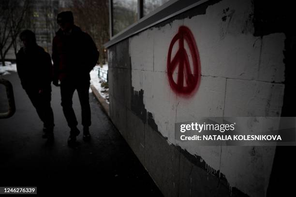People walk past a peace symbol painted on a building in Moscow on January 16, 2023. - Despite strict government censorship and the threat of jail,...