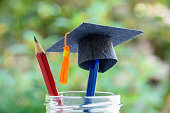 Black graduation cap or a mortarboard, blue and red pencils in a bottle