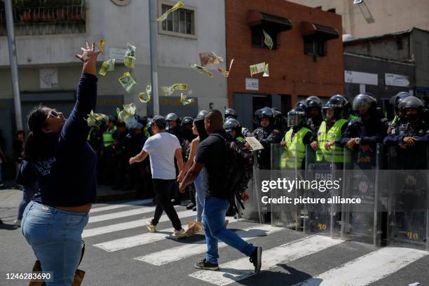 January 2023, Venezuela, Caracas: A woman throws a pile of banknotes in the air in front of policemen, which have radically lost value because of...