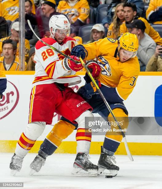 Elias Lindholm of the Calgary Flames battles for the puck against Jeremy Lauzon of the Nashville Predators during an NHL game at Bridgestone Arena on...