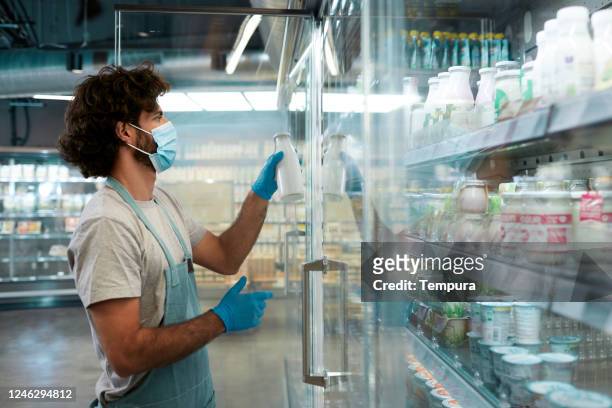 ein argentinischer mitarbeiter eines lebensmittelgeschäfts, der lebensmittel im kühlschrank aufbewahrt - essenzielle berufe und dienstleistungen stock-fotos und bilder