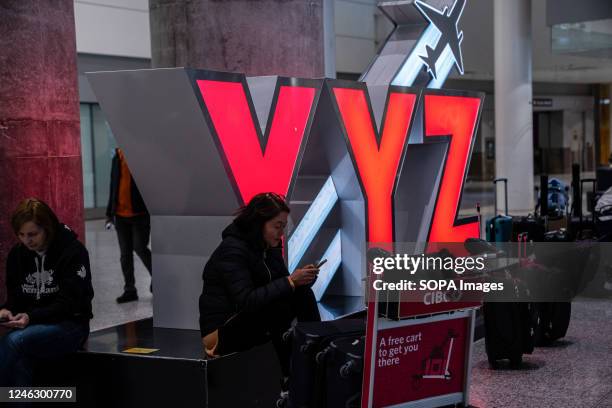 Woman with luggage sits under a bright red YYZ sign at the YYZ Toronto Pearson International Airport. Canadian travel has faced a series of...