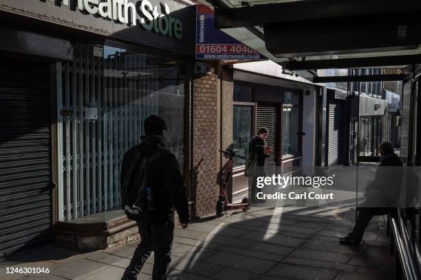 People wait at a bus stop next to boarded up shops in the town centre on January 17, 2023 in Northampton, England. Over 17,000 High Street shops...