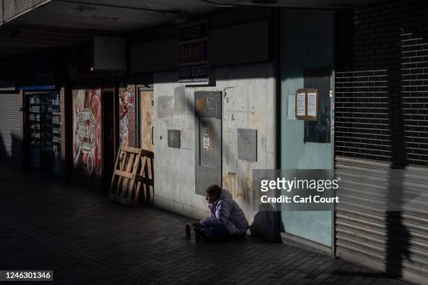 Homeless woman begs outside boarded up shops in the town on January 17, 2023 in Northampton, England. Over 17,000 High Street shops closed for good...