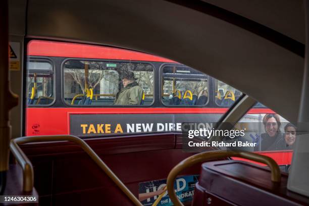 Seen from another bus, an elderly passenger sits on the top deck of a London bus, where advertising is seen beneath him, on 17th January 2023, in...