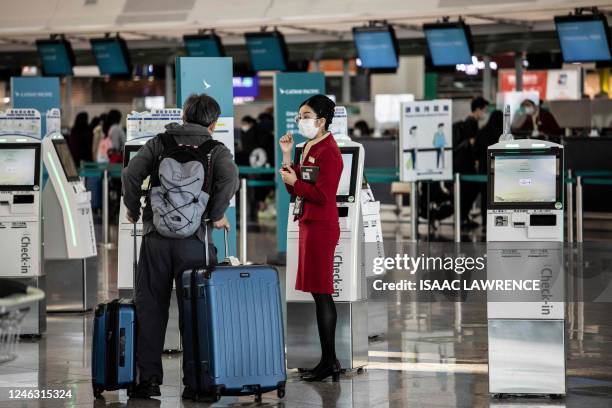 This picture taken on December 23, 2022 shows a ground staff member helping a passenger next to a self check-in kiosk at Hong Kong International...