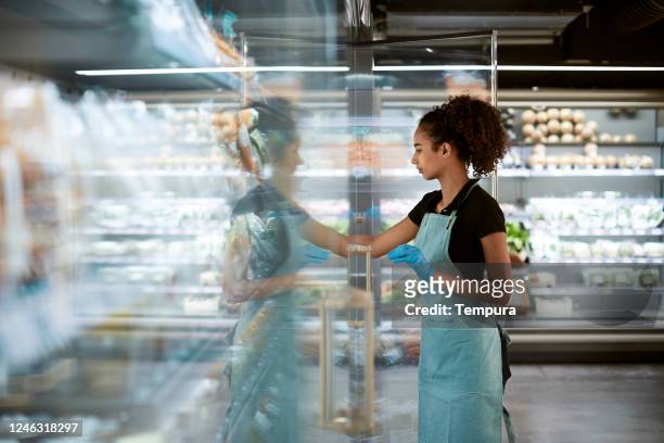 ein mitarbeiter eines lebensmittelgeschäfts passt die produkte im kühlschrank an. - supermarket refrigeration stock-fotos und bilder