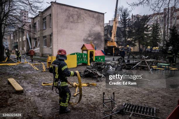 Firemen roll up hoses in front of debris as emergency service workers respond at the site of a helicopter crash on January 18, 2023 in Brovary,...