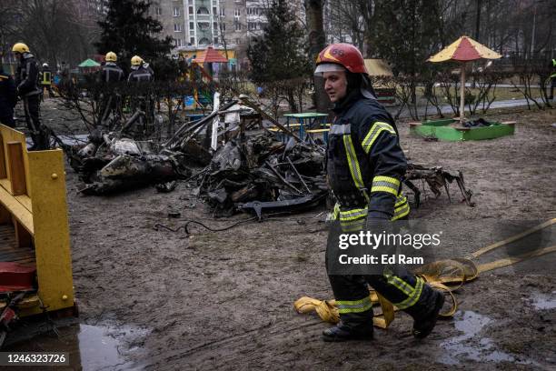 Firemen roll up hoses in front of debris as emergency service workers respond at the site of a helicopter crash on January 18, 2023 in Brovary,...