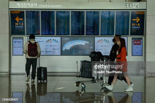 Passengers with luggages walk in front of a flight information board at Incheon International Airport on January 18 South Korea. According to Incheon...