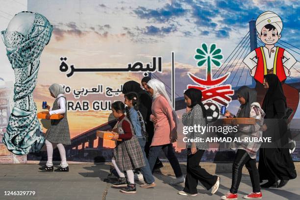 Women and children walk past a giant banner advertising for the 25th Arabian Gulf Cup football championship erected along the waterfront of the Shatt...