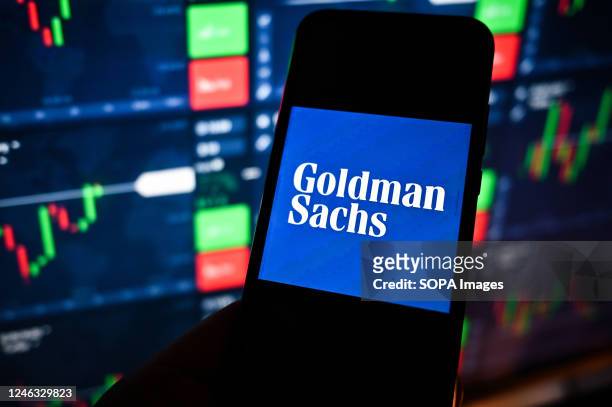 In this photo illustration a Goldman Sachs logo is displayed on a smartphone with stock market percentages on the background.
