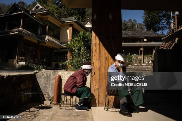 This photo taken on January 11, 2023 shows ethnic Blang women, who are Covid-19 coronavirus patients, on IV drips as they sit in the compound of a...