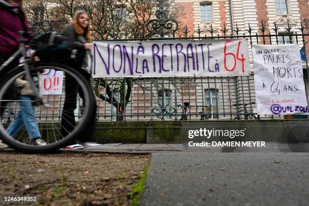 People walk past a banner hanging from the fence of the e Lycee Zola school that reads, ' No to retirement at 64', as French trade unions call for a...