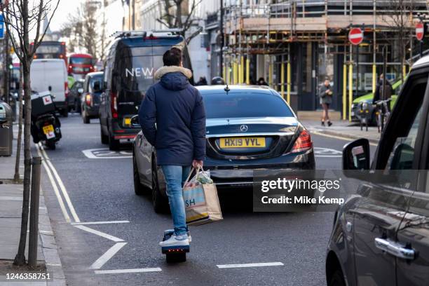 Man with shopping bags passes on a single wheeled electric skateboard personal transporter on 13th January 2023 in London, United Kingdom. Onewheel...