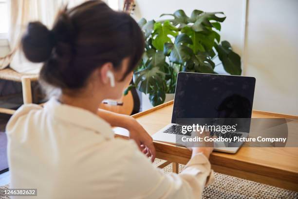 young woman video chatting online with a laptop at home - over the shoulder view stock pictures, royalty-free photos & images