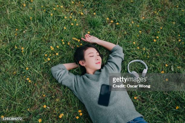 young woman lying down in meadow with smartphone and headphone - woman taking a nap stock-fotos und bilder