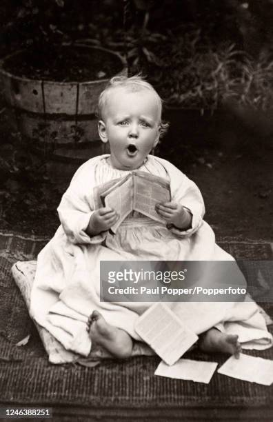 Small child with bare feet sitting on a pillow singing from a tattered hymnbook, circa 1920.