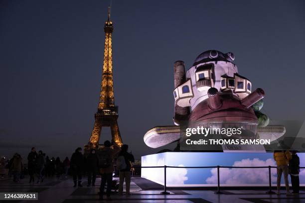 Members of the public stand in front of the Eiffel Tower and near an inflatable installation picturing Japanese director, animator and manga artist...