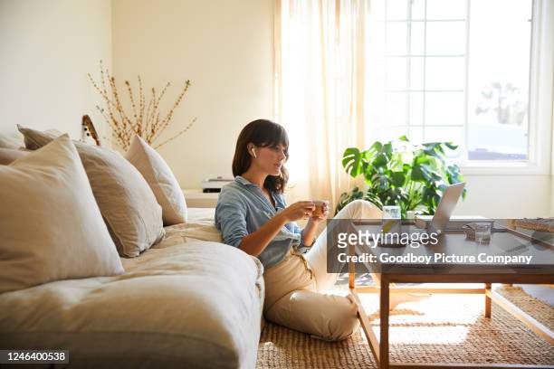 vrouw die iets op laptop in haar woonkamer stroomt - coffee table stockfoto's en -beelden