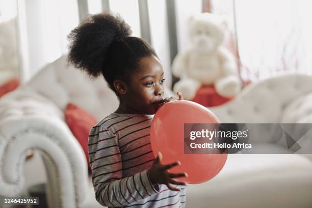 beautiful young girl blowing up a red balloon - inflar fotografías e imágenes de stock