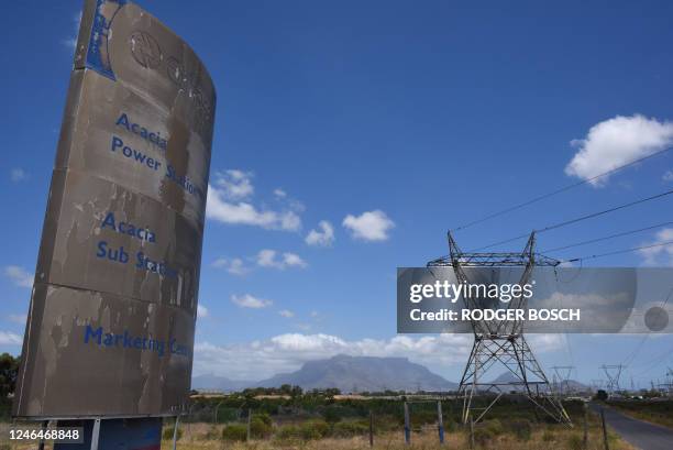 Dilapidated sign for Eskom, the South African electricity authority, stands next to electricity pylons and Table Mountain in the distance near Cape...