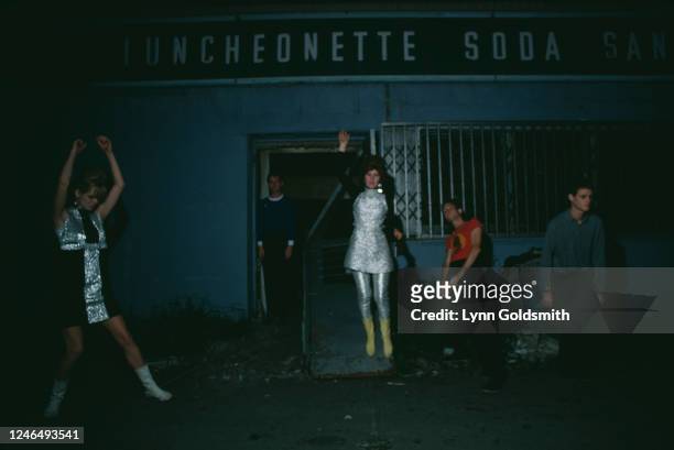 Nighttime portrait of members of American New Wave group the B-52s as they pose outside a luncheonette, August 1978. Pictured are, from left,...