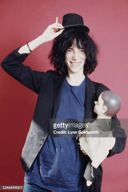 Portrait of American Rock musician and poet Patti Smith as she poses with a ventriloquist's dummy in one hand and the dummy's hat, held over her...