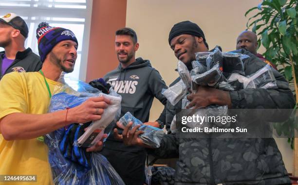 Carrying donated clothing, Christian Espinoza, left, exchanges greetings with Ravens kicker Justin Tucker, center, and quarterback Lamar Jackson...