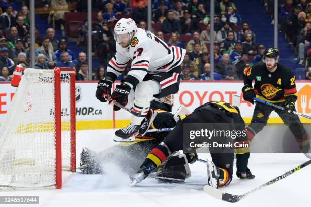 Jason Dickinson of the Chicago Blackhawks jumps over Collin Delia and Tyler Myers of the Vancouver Canucks during the second period of the NHL game...