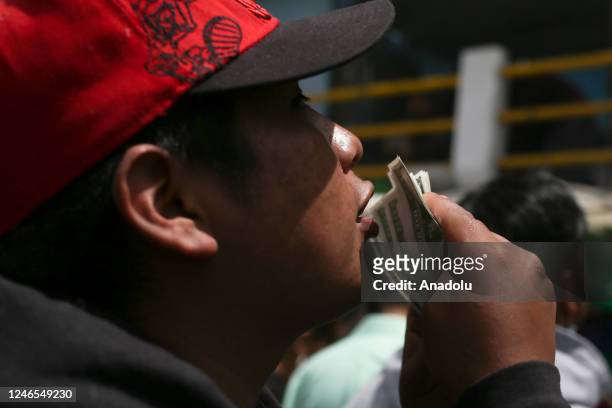 Man blows replicas of Bolivian dollars and pesos stacked on the ground during the Alasitas fair in La Paz, Bolivia on January 24, 2023. Every January...