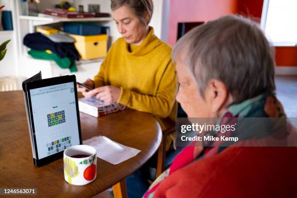 Elderly woman plays Wordle on her iPad tablet at the kitchen table of her daughter's home and struggles to find the first green letters on 21st...