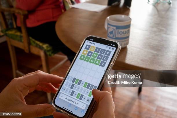 Woman plays Wordle alongside her mother on her smartphone at the kitchen table of her home and struggles to find the correct final word on 21st...