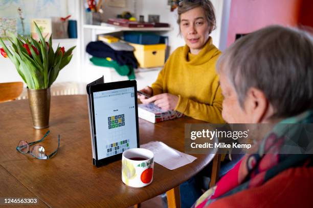 Elderly woman plays Wordle on her iPad tablet at the kitchen table of her daughter's home and struggles to find the first green letters on 21st...
