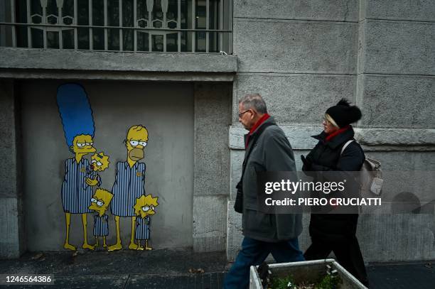 People walk past a mural by Italian street artist AleXsandro Palombo entitled "Track 21 The Simpsons deported to Auschwitz" on January 26, 2023 near...