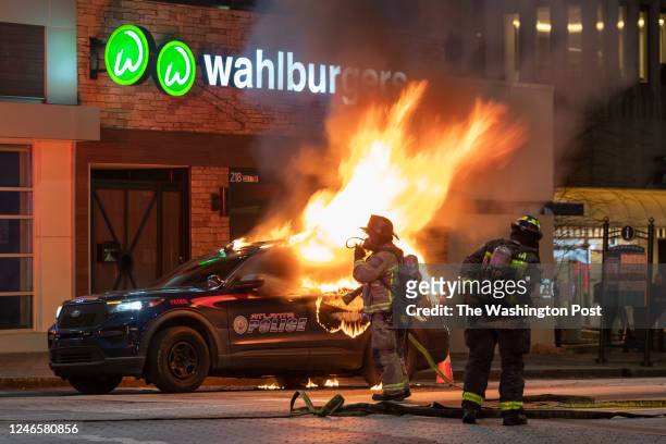 Firefighters are seen in front of a burning police vehicle during a protest following the shooting death of Manuel Teran during a police raid on...