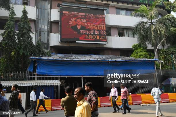 Pedestrians walk past an electronic signage displaying news on the Adani Group at the Bombay Stock Exchange building in Mumbai on January 27, 2023. -...