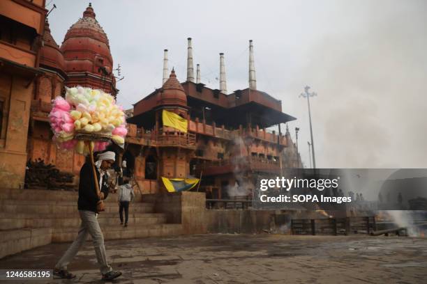 Street vendor selling cotton candy walks past Manikarnika Ghat on the banks of the river Ganges in the northern Indian city of Varanasi in Uttar...