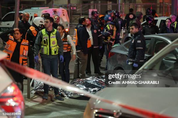 Israeli emergency service personnel and security forces stand near a covered body at the site of a reported attack in a settler neighbourhood of...