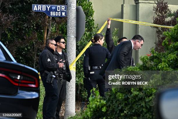 Police officers lift police tape for an investigator after an early morning shooting that left three people dead and four wounded in the Beverly...