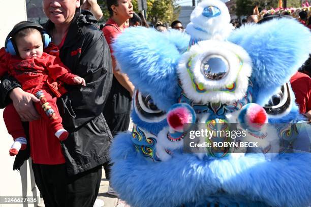 Person carries a baby wearing ear protection past lion dancers at the 124th annual Golden Dragon Lunar New Year Parade, to celebrate the year of the...