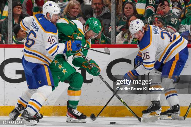 Ilya Lyubushkin and Rasmus Dahlin of the Buffalo Sabres battle for the puck with Marcus Foligno of the Minnesota Wild during the game at the Xcel...