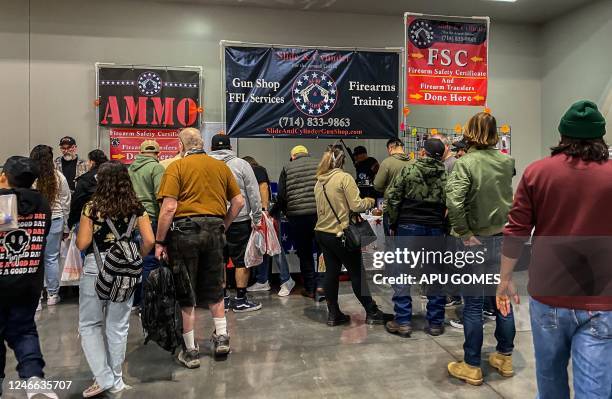 People stand in front of a gun shop and firearms training booth at the Crossroads of the West Gun Show at the Convention Center in Ontario,...