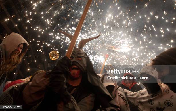 January 2023, Spain, Palma: A man dressed as a demon, holding a firework, walks among the people during the traditional Correfoc at the end of the...